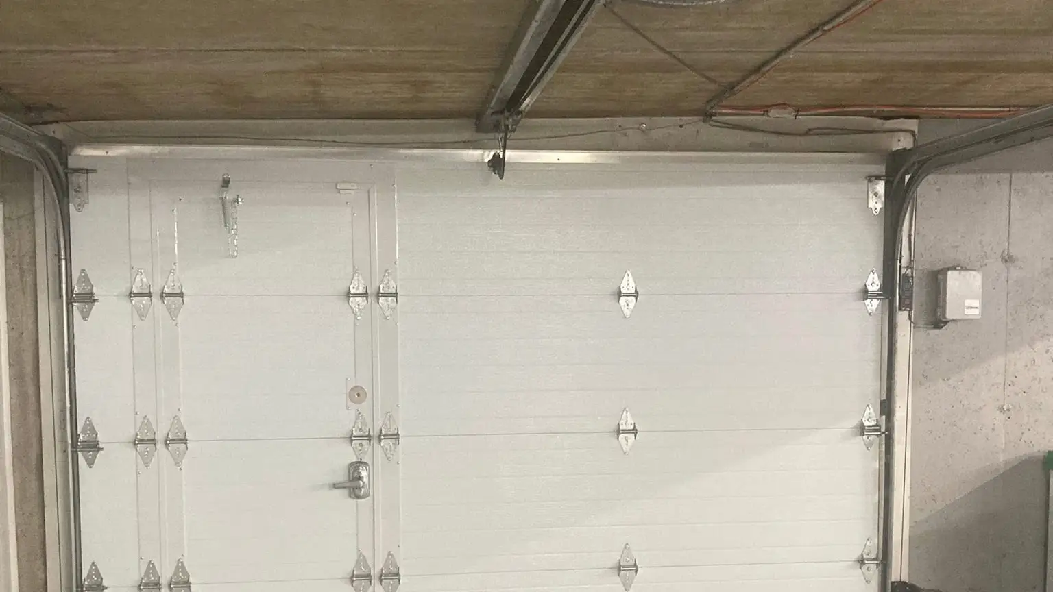Porte de garage blanche vue de l'intérieur, ses rails et son ouvre-porte
