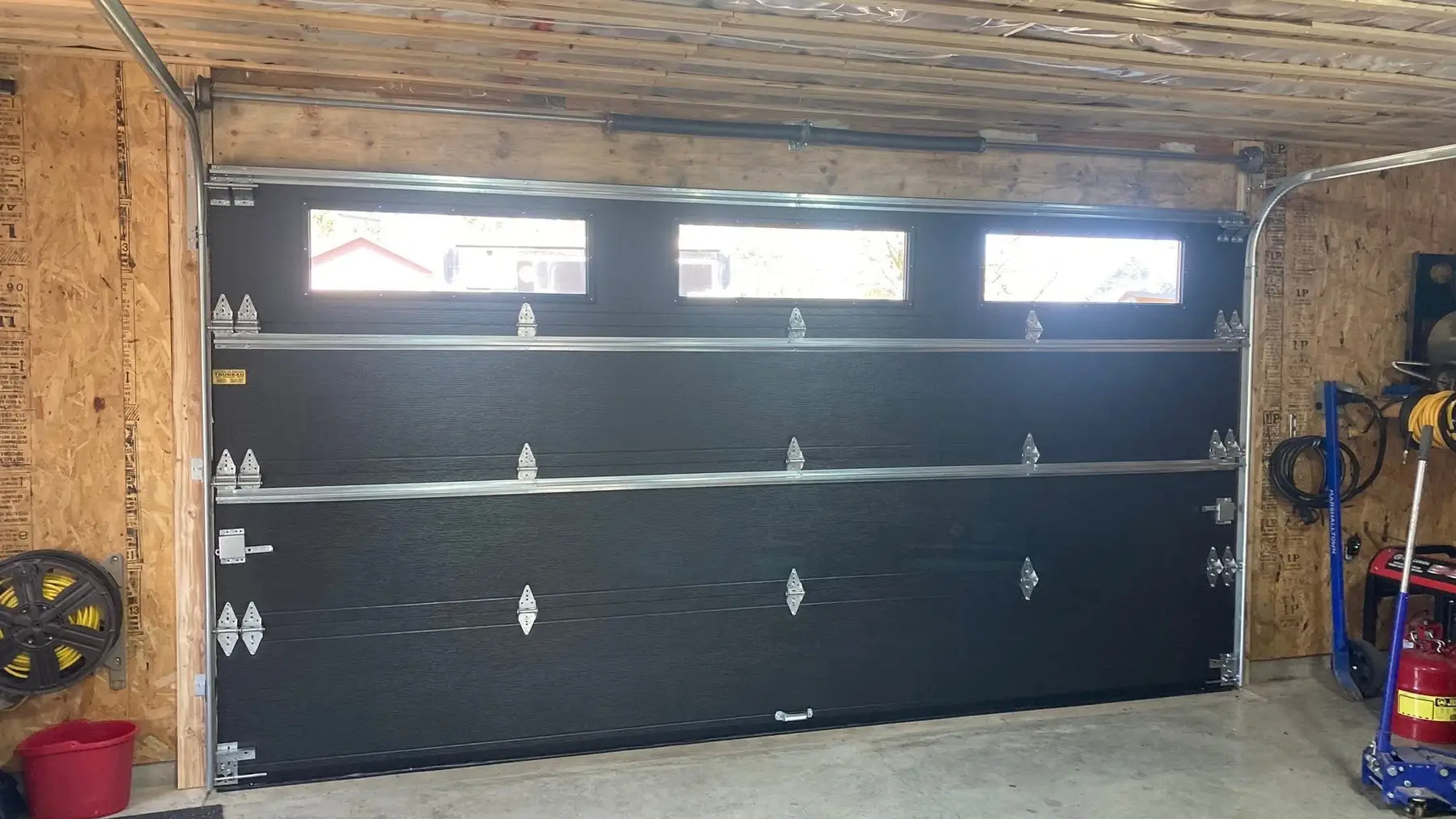 Porte de garage noire vue de l'intérieur, avec ses rails et sa quincaillerie